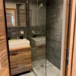 Salle de bain moderne rénovée équipée d'une douche à l'italienne, utilisation de produit noble tel que le bois et le carrelage.