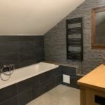 Salle de bain moderne rénovée avec des carreaux en pierre, une baignoire encastrée et un radiateur sèche-serviettes noir.