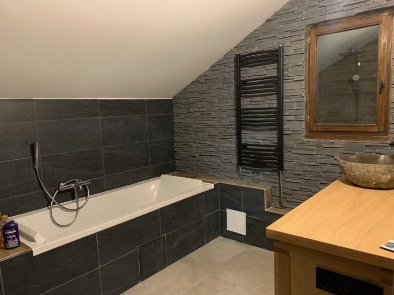 Salle de bain moderne rénovée avec des carreaux en pierre, une baignoire encastrée et un radiateur sèche-serviettes noir.