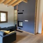 Salon moderne avec un canapé gris, des accents de bois, une grande fenêtre et une cheminée encastrée.