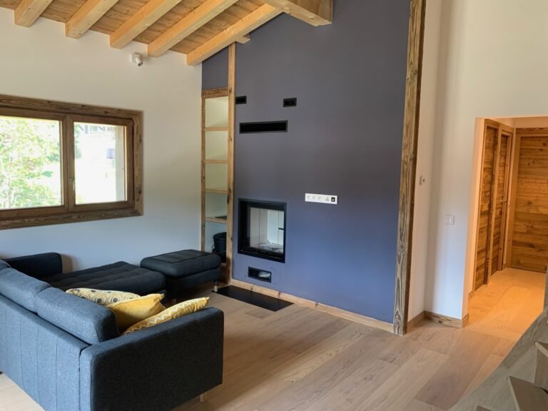 Salon moderne avec un canapé gris, des accents de bois, une grande fenêtre et une cheminée encastrée.